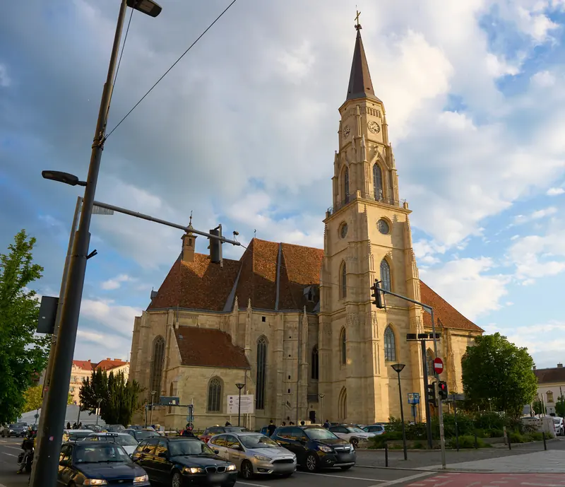 Biserica Sfântul Mihail din centrul Clujului, văzută din stradă, cu mașini la semafor